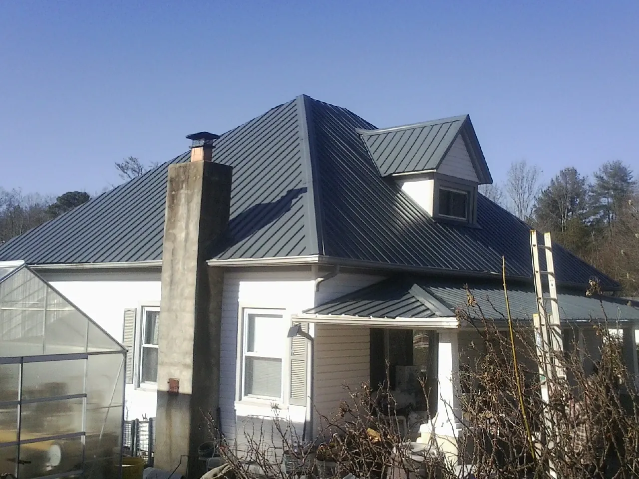 Dark blue standing seam metal roof on a white farmhouse with dormer — Slate & Tile Roof Repair by Roofing Brothers in Four Oaks