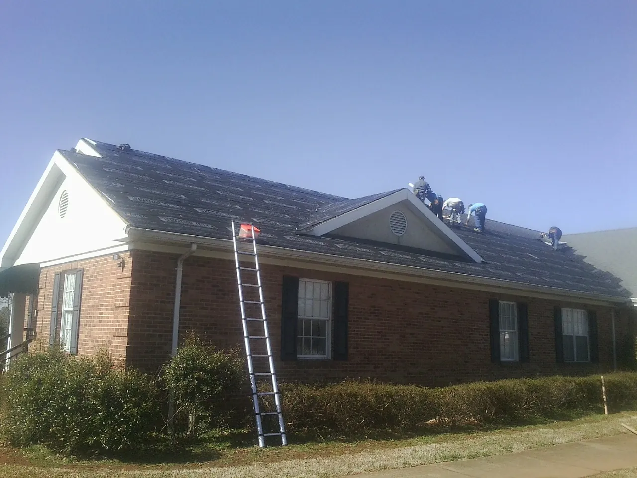 Crew tearing shingles off a brick ranch roof with a ladder set — Emergency Roof Repair work by our crew in Four Oaks
