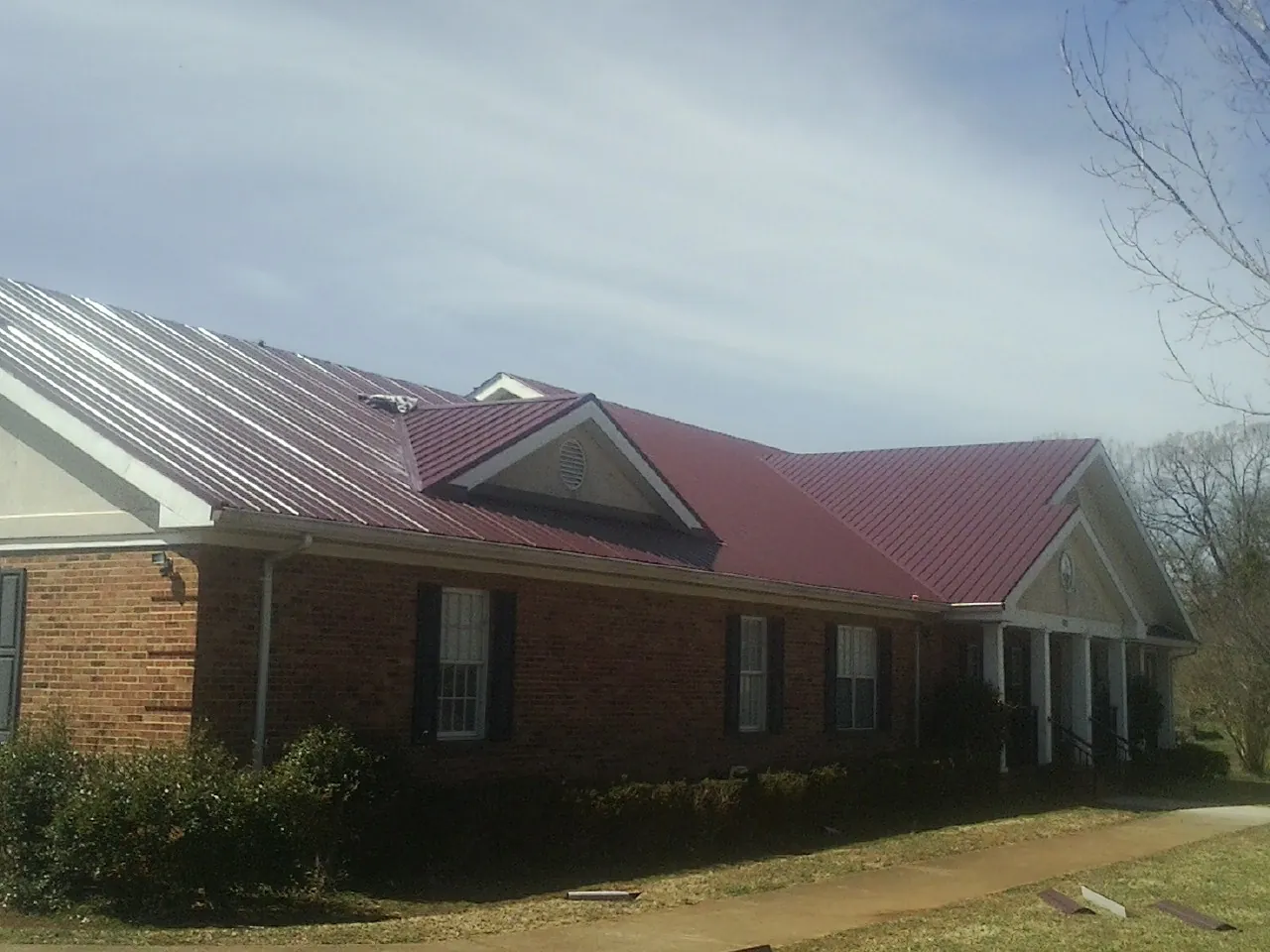 Red metal roof with gabled entries on a long brick building, from a Hail Damage Roof Repair job in Four Oaks