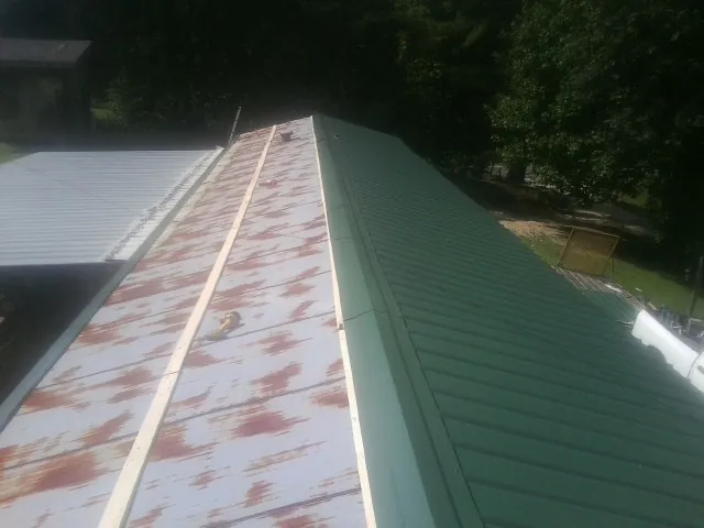 Old rusted panels beside newly installed green metal roofing — Wind Damage Roof Repair by Roofing Brothers in Four Oaks