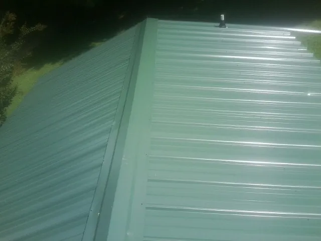 New green metal panels meeting at the ridge of a roof — Flat Roof Repair work by our crew in Four Oaks