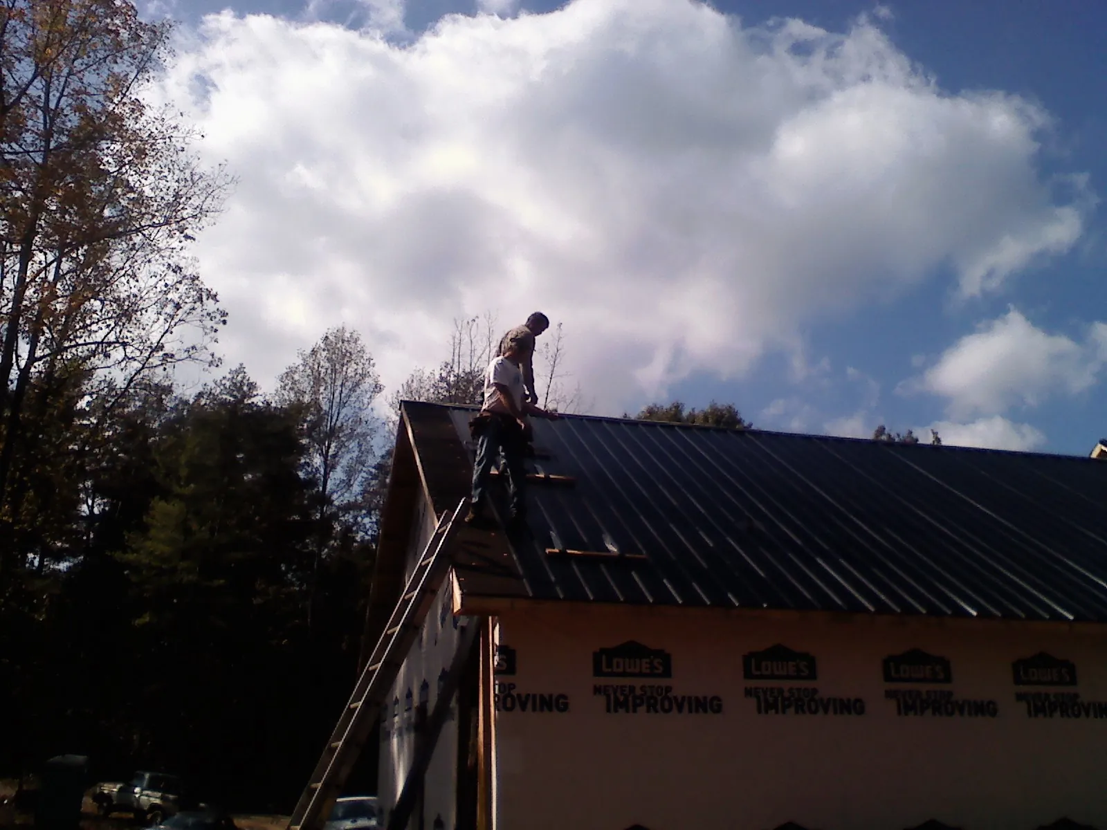 Roofer fastening dark metal panels high against a cloudy sky, from a Roof Inspection job in Four Oaks