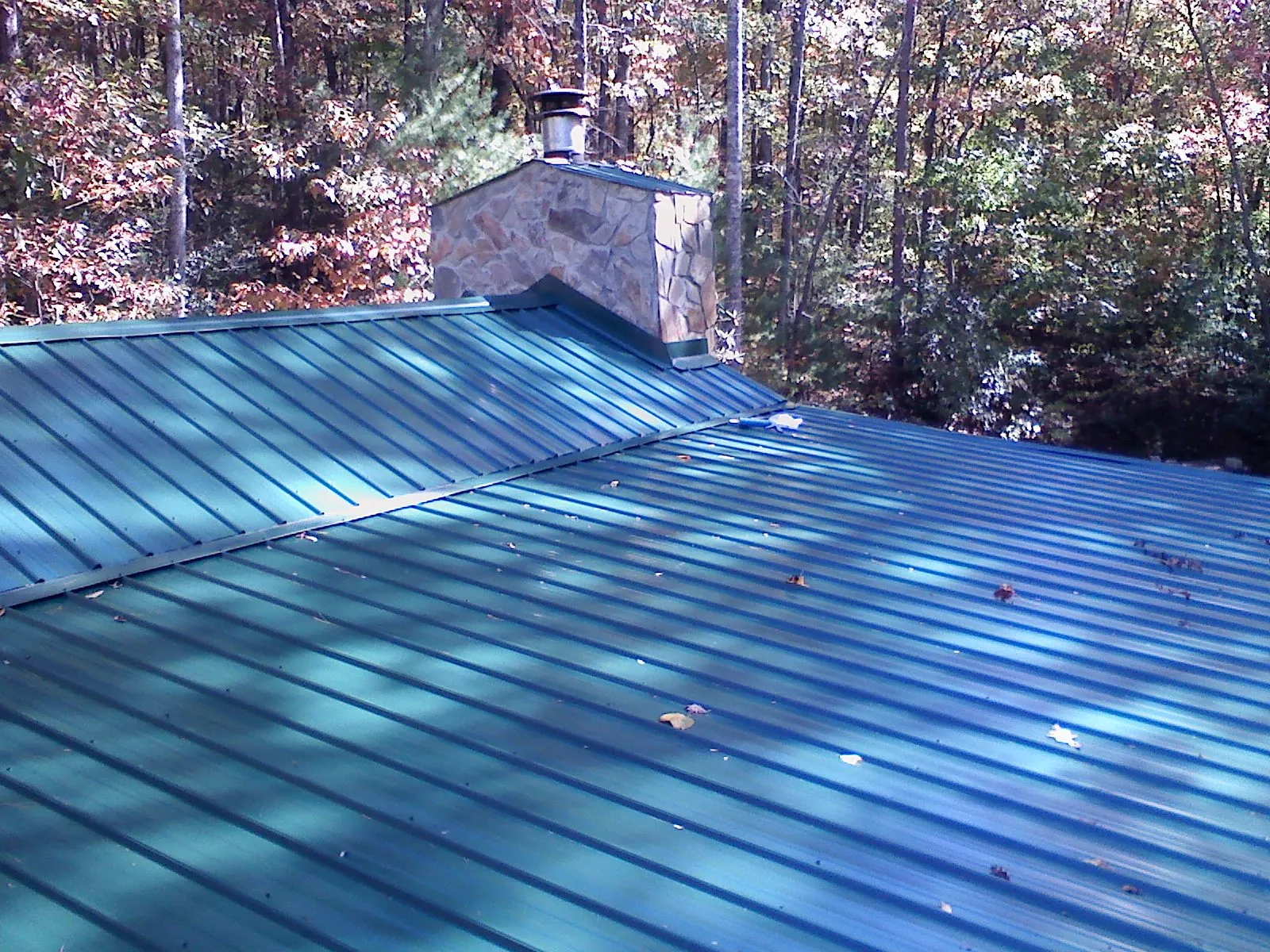 New green metal roof and stone chimney surrounded by autumn woods in Four Oaks