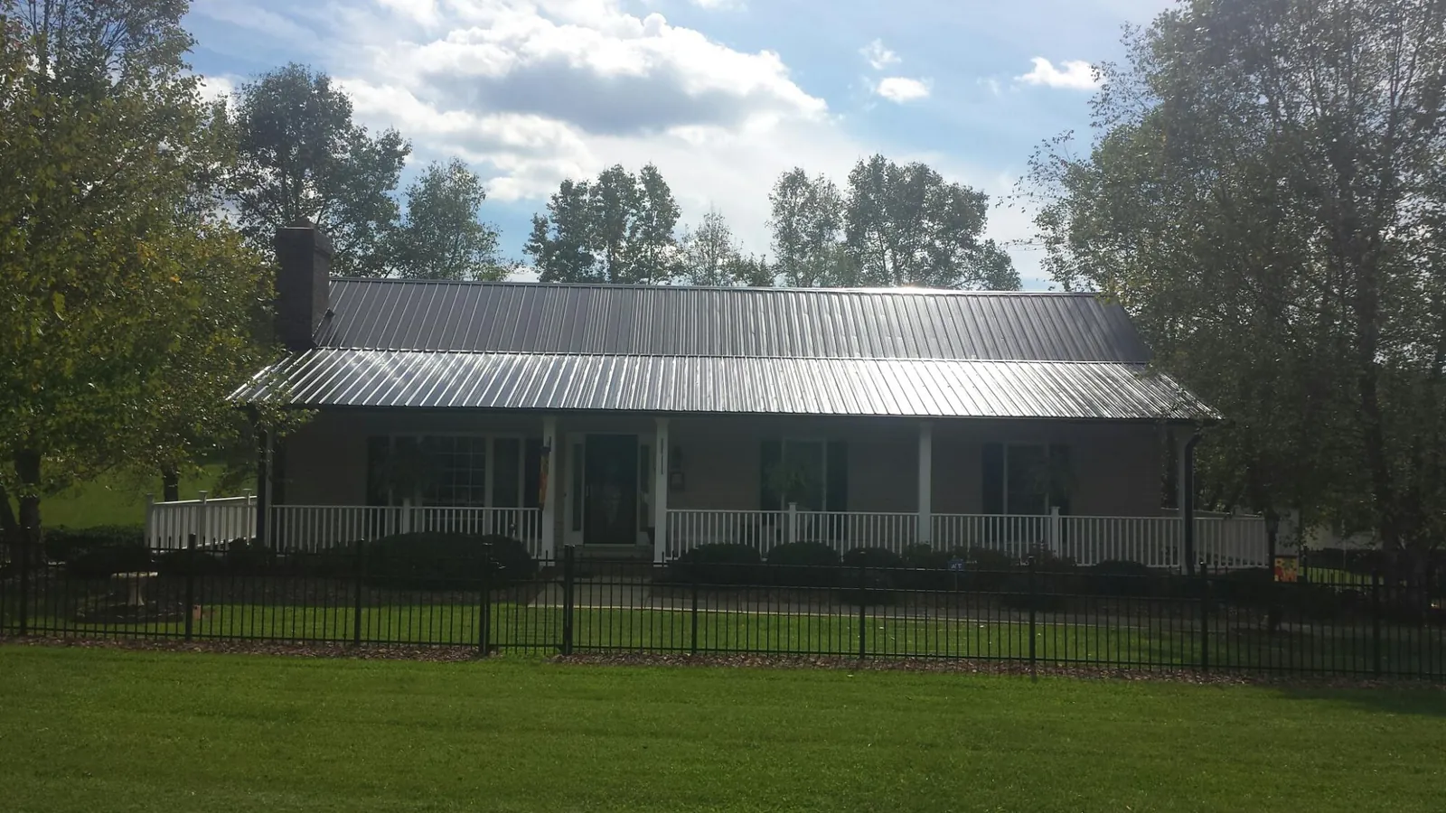 Gray metal roof on a brick ranch with a full width front porch — Gutter Guard Installation work by our crew in Four Oaks