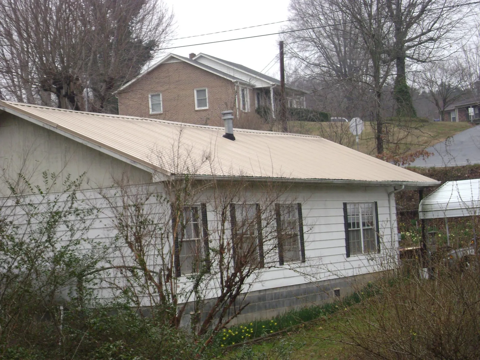 Tan metal roof on a white sided house set into a hillside — Commercial Roofing by Roofing Brothers in Four Oaks